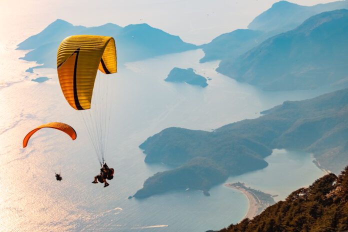 Ilustrácia muža a ženy, ktorí zažívajú paragliding s nádherným výhľadom na krajinu pod nimi.