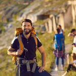 Usmievajúci sa turista s batohom a výbavou na horskej túre, pripravený na ďalšie dobrodružstvo.