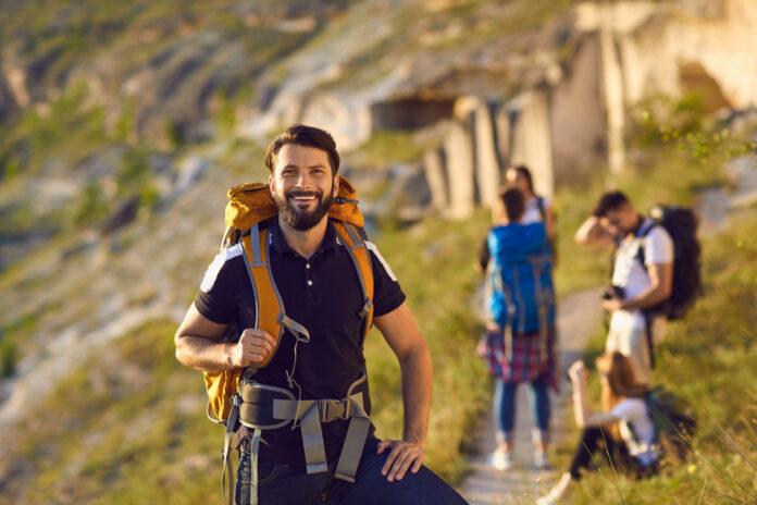 Usmievajúci sa turista s batohom a výbavou na horskej túre, pripravený na ďalšie dobrodružstvo.