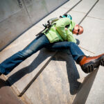 Muž v turistických topánkach a mestskom oblečení leží na betónových schodoch v meste.