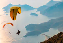 Ilustrácia muža a ženy, ktorí zažívajú paragliding s nádherným výhľadom na krajinu pod nimi.